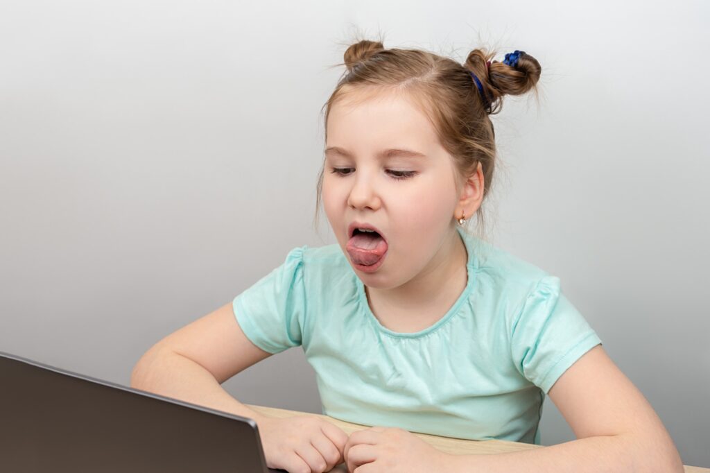 Speech training concept. Little girl uses a laptop to study at home with a teacher, a speech therapi